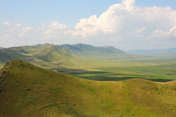 Picturesque steppe surrounded by high mountains and hills under a clear summer sky.
