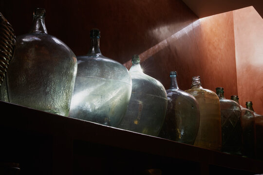 Cinco garrafas antiguas de vidrio iluminadas por un rayo de luz solar.