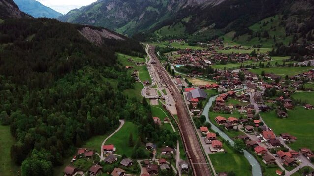 Flight over a Swiss mountain valley around train tracks with a car train for queuing up for L&ouml;tschberg Tunnel