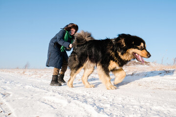 Boy have fun, laugh and walk with his big black dog on winter background. Family winter activity with pet on sunny day outdoor. Happy moments of childhood
