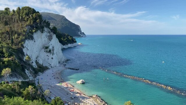 Splendid view from Piazza Nuova of Numana at the Friar's beach (Spiaggia del Frate) with its sandy beach and parasols, pure emerald waters and few people under impressive mountains topped by greenery