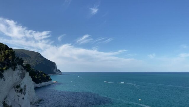 Bright view from Piazza Nuova of Numana at Mount Conero (Monte Conero) with the delicately rippling Adriatic Sea at its feet and different fast-moving vehicles skimming and leaving white trails