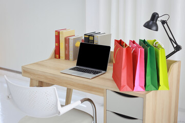 Fototapeta na wymiar Shopping bags on wooden working table with computer black blank screen and books in room house indoor. Free space for your advertisement