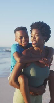Vertical video of happy african american mother and son having fun on beach