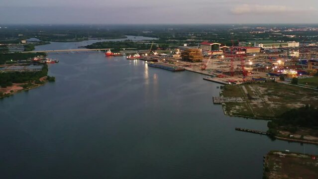 Dusk aerial tilt up shot capturing massive fabrication yard, plant and marine shipyard at Kampung Acheh Lumut port industrial park, ship building and repair hangars and hardstands, Perak, Malaysia.