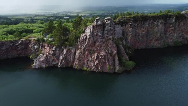 Aerial push in of old Irish quarry overlooking green fields