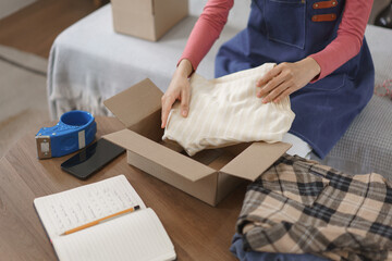 Online shopping business concept, Women entrepreneur packing clothes in box for delivery to client