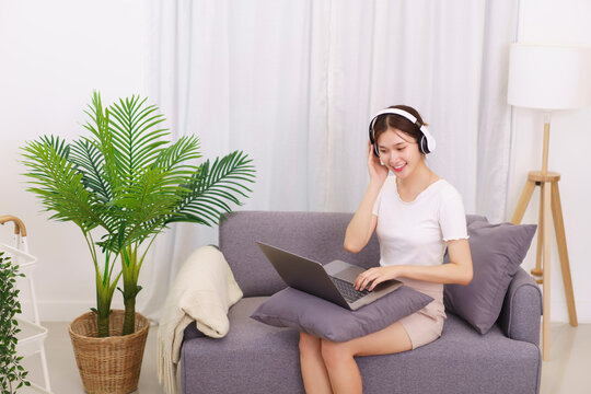 Lifestyle in living room concept, Young Asian woman in headphone to watching movie on laptop