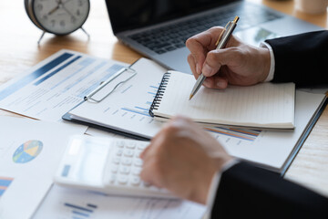 Asian business woman Calculate earnings with a calculator. Taking notes in a notebook for financial reporting or profits. Income tax. Management concept. Accounting and finance.