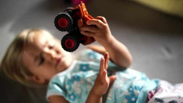 Little girl playing with a toy car lying on the bed