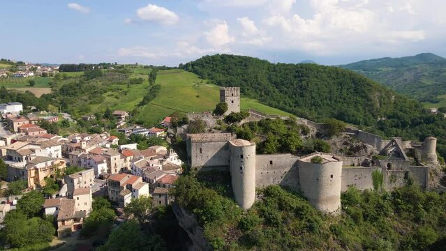 Drone shot flying away from a medieval castle on top of a cliff with tourists climbing to the summit and birds flying by. This ancient castle is located in Abruzzo Italy and is called Roccascalegna.