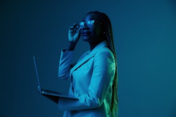 African African woman with laptop in glasses on a blue background in neon light, color mixed light. Data storage cyber security, hacker, big data.