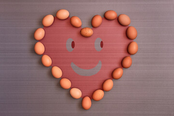 Eggs placed in the shape of a heart with a happy face smiling to communicate that they are good for the heart and health . View from top