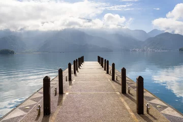 Fototapeten Pier Large blue lake surrounded by mountains with pier in the morning at sun moon lake of Taiwan  © leungchopan