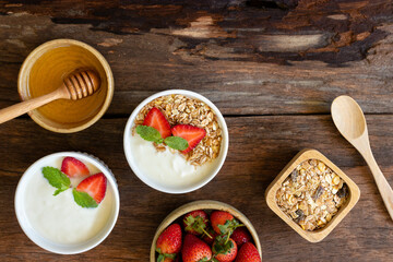 Strawberry yogurt in a wooden bowl with granola, honey, mint and fresh strawberry on wooden background. Health food concept..