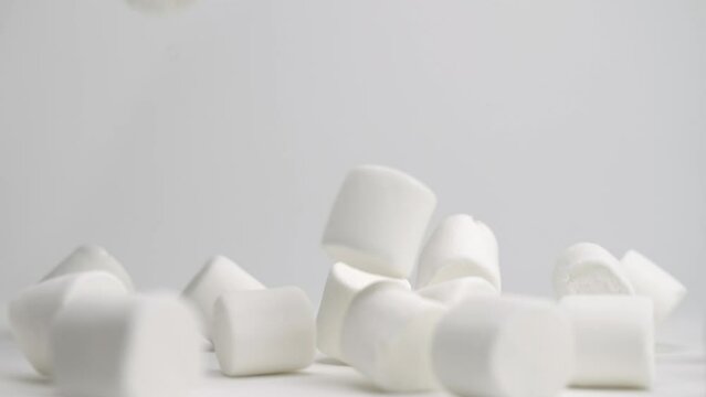 White squishy jumbo marshmallows falling onto white table top and bouncing around into a pile in slow motion