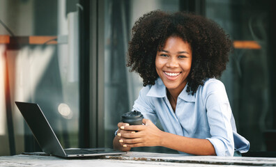 Young smiling african american woman sitting at desk in co-workspace, looking at camera.