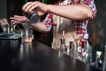 bartender pouring a cocktail from a shaker into a glass.