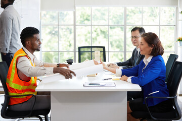 engineer holding white paper or blueprint and talking with colleagues in the office