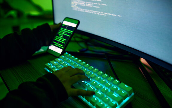 Phone, neon and hands typing on a keyboard while doing website design or coding on a computer at night. Technology, cellphone and male coder working late on webdesign project in office in the evening