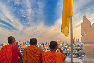 Three Buddhist monks looking at skyline of Bangkok, Thailand, at