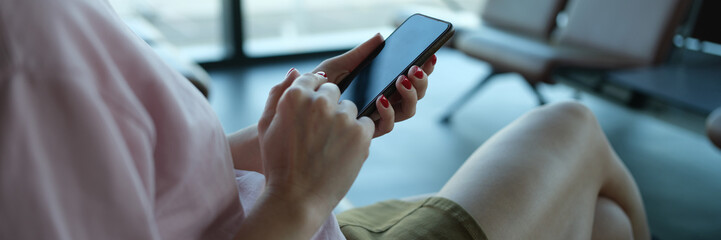 Woman traveler with smartphone in her hands sits in departure area at airport or train station