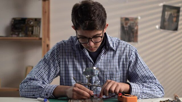 Young student learning electronics testing circuit board with multimeter while working at home.
