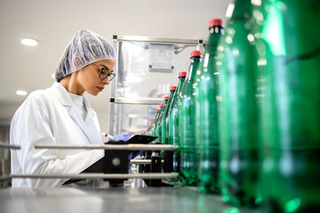 Naklejka na ściany i meble Female technologist working in PET bottling factory controlling production of drinking water and packaging.