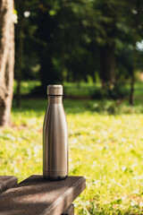 Water bottle. Reusable steel thermo water bottle on wooden bench. Sustainable lifestyle. Plastic...