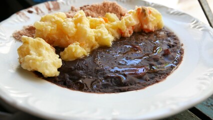 A lunch plate: cooked beans (Brazilian feijoada); cooked cassava flour; potato salad mixed with...