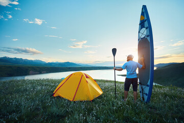 Man with SUP board near lake at sunset - 571466949