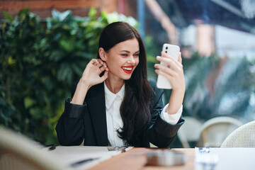 Stylish woman blogger sits in a cafe with a phone in her hands reads a message, mobile communication and internet on a journey, video call, freelance work online, smile with teeth