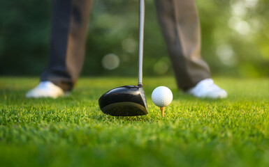 Close-up of golf ball on tee and drivers with golfer ready to tee off.