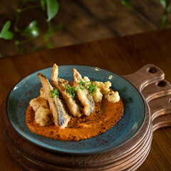 Fried fish pieces with vegetables and vegetable puree. Plate with dish on wooden planks on table. Serving food in restaurant. Vegetarian menu. Side view. Soft focus. Copy space. 