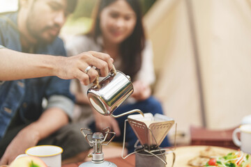 Asian couple drip coffee in the camp enjoying camping outdoors in nature. Man traveler hands holding cup of coffee.