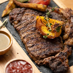 Steak with sauce and vegetable garnish on plate. Meat is served with sauces. Plate with dish on wooden table. Dinner at restaurant. Soft focus. View from above. Close-up. 