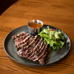 Juicy medium rare meat steak. Meat is cut into pieces and served on plate with sauce and lettuce leaves. Dinner at restaurant. Wooden table. Top view. Soft focus.