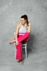 Cute woman in tank top and wide pink trousers sitting on chair