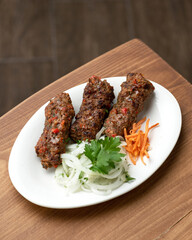 Lula kebab with side dish of fresh vegetables on white plate. Asian cuisine, Oriental cuisine. Dish on white plate on wooden table. Pickled onions and carrots. Soft focus. View from above. 