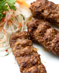 Grilled lula kebab with side dish of fresh vegetables on white plate. Asian cuisine, Oriental cuisine. Minced meat products. Pickled onions and carrots. Close-up. Soft focus. View from above. 