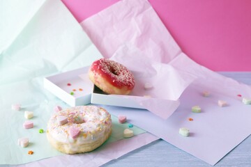 Freshly baked donuts glazed with various pink shades and sprinkled with caramel hearts, lilac shade wrapping paper on the table, Donut Day 