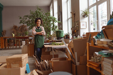 Attractive smiling florist stands with crossed arms on background of her own floral decor studio