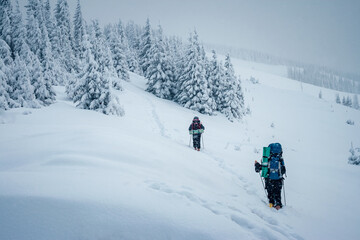 Hikers with backpacks make their way through snowy slopes on a frosty day.