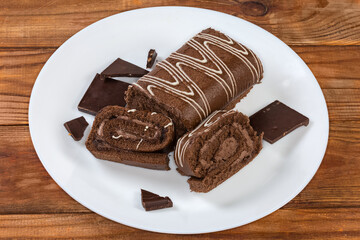 Partly sliced chocolate roll and dark chocolate pieces on dish