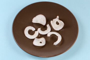 Round dried coconut pulp slices on dish on blue background
