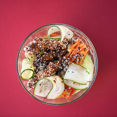 Chicken with teriyaki sauce and garnish of carrots, peppers and cucumbers. Asian dish. Eastern cuisine. Dish in transparent bowl. Raspberry background. Top view.
