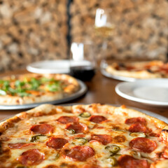 Three pizzas on table in pizzeria. Lunch at pizzeria. Pepperoni pizza. Wooden table. Blurred background. Close-up. Soft focus. Side view. 