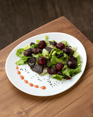 Salad with beets. Boiled beets, liver, lettuce, herbs and sauce. Dish on white plate on wooden table. Healthy diet. Low calorie food. View from above. Copy space. 