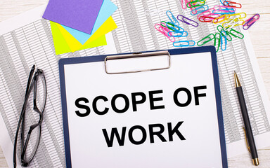 A notepad with the text SCOPE OF WORK, a pen, reports, bright stickers, paper clips and glasses lie on a white office table. Top view with copy space, flat lay.