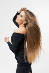 Fototapeta premium Portrait of a young woman in a black dress with long well-groomed hair. Hairstyle for photography